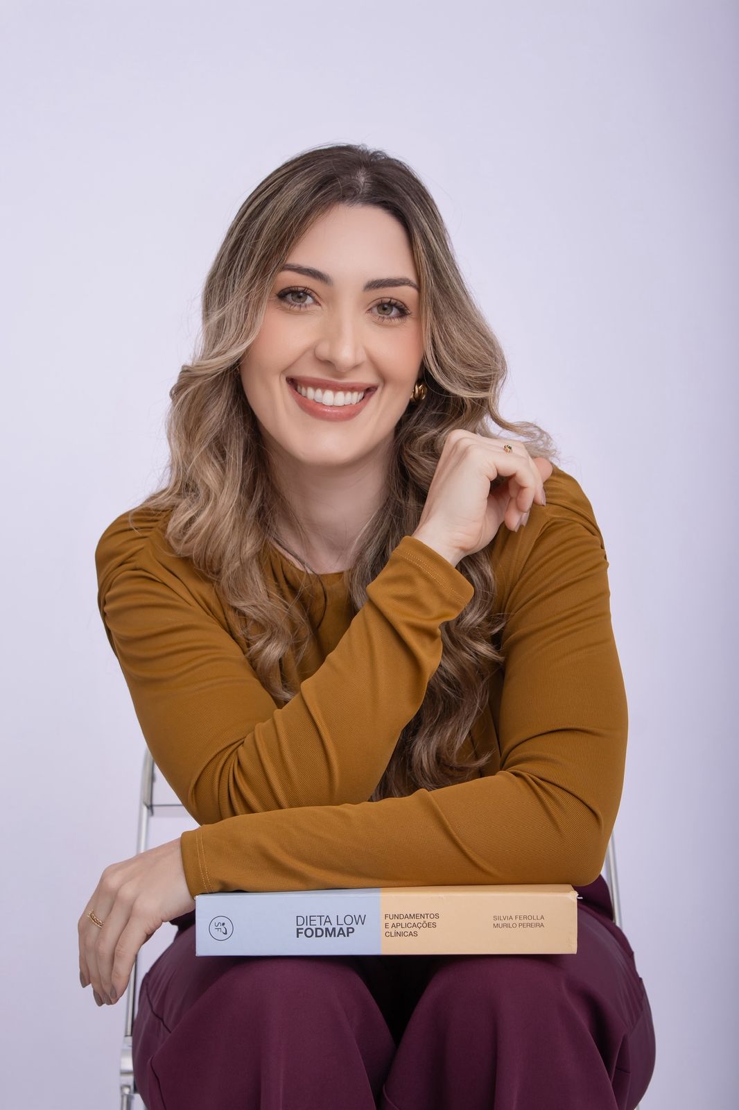 Mariana Micheleto sorrindo, apoiada no livro Dieta Low FODMAP